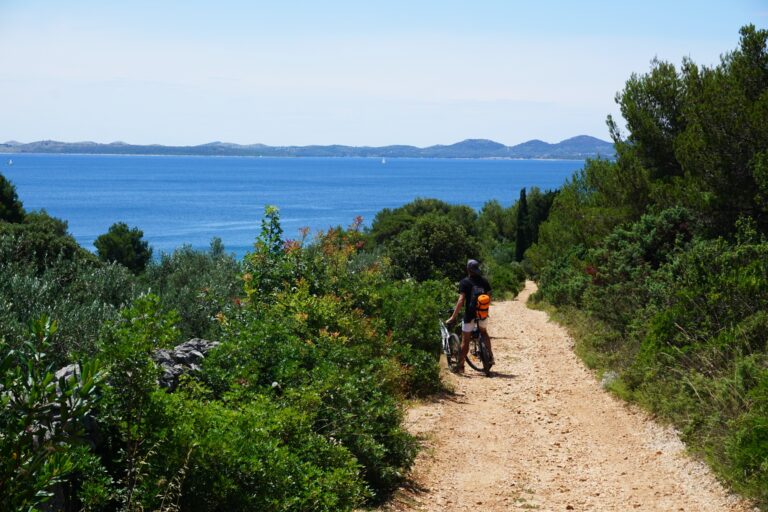 A young man on an MTB on a gravel trail looking at a view over the sea